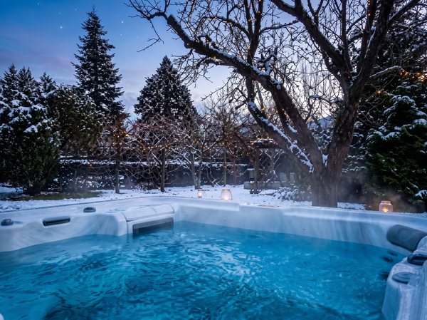 Une photographie améliorée d'un spa extérieur fumant et éclairé par des lumières cyan, contrastant avec un paysage d'arrière-plan enneigé et détaillé sous un ciel nocturne étoilé